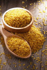 Composition with a bowl and spoon of uncooked bulgur on a table