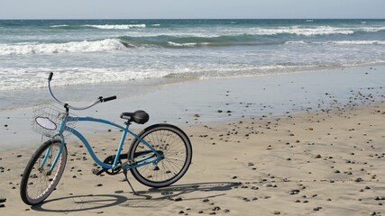 Fototapeta premium Blue bicycle, cruiser bike by ocean beach pacific coast, Oceanside California USA. Summertime vacations, sea shore. Vintage cycle on sand. Clear sky and water waves. Waterfront summer near Los Angeles