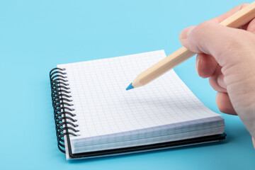 Woman's hand writing in notebook on blue background. Working place and planning concept.