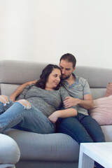 Pregnant wedding couple sitting on a sofa looking at each other and smiling