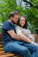 Fototapeta premium Pregnant couple sitting on a bench and posing in a park