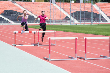 Fototapeta premium Two female sportswomen are jumping over an obstacle. Running with hurdles. Active lifestyle