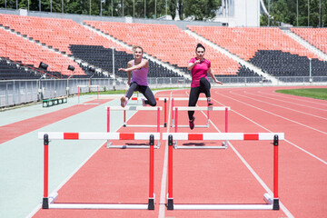 Two female sportswomen are jumping over an obstacle. Running with hurdles. Active lifestyle