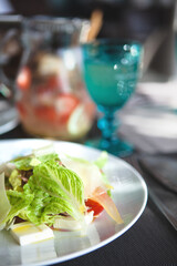 Healthy eating scene. Close up of gourmet delicious salad with fresh lettuce, cherry tomatoes and cheese on a white plate. Front view, selective focus.