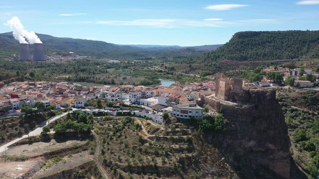 Aerial view of historical Spanish town of Cofrentes with medieval castle on top of basalt rock and modern nuclear power plant cooling towers on background, Valencia, Spain. High quality 4k footage