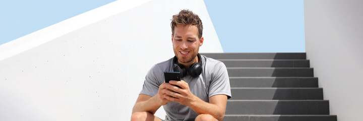 Young fit man using mobile phone app for online streaming of music listening with wireless...