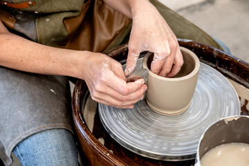 Woman working on the potter's wheel. Ceramist young woman making clay product on pottery lathe in studio. Close up of female hands working on potters wheel