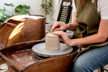 Woman working on the potter's wheel. Ceramist young woman making clay product on pottery lathe in studio. Close up of female hands working on potters wheel