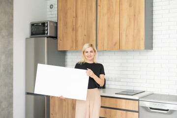 White canvas in female hands with gray wall background. Woman hanging blank picture mockup on wall...