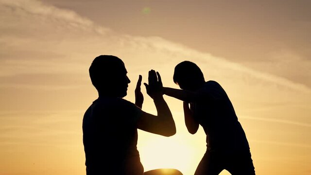 Happy family in park. Father and son boxing in park at sunset. Silhouette of family at sunset. Father helps his son to box. Family box. Sporty happy family concept. Father and son boxing in park