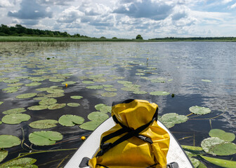 landscape with a river, in the foreground a sup board with a yellow, waterproof rubber bag