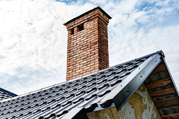 Brick chimney pipe on metal roof of house.