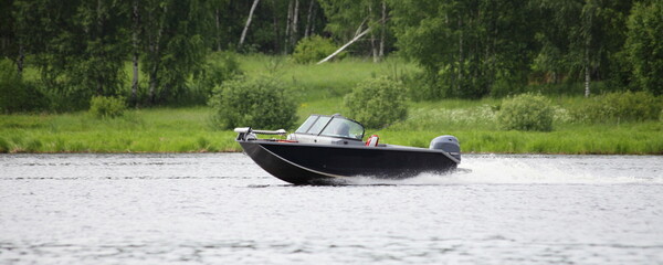 Fast gliding Russian fishing motor boat side view on green trees on far shore background in Tver ragion at summer day, active recreation boating tourism on Volga river