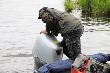 Boater man hands looking on the the gray hood of a 50 hp four stroke outboard motor on transom of...