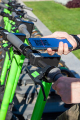 A young man rents an electric scooter by scanning the QR code with a smartphone