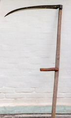 Old scythe with wooden snaith against the white wall