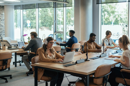 Mixed-Race Team  Sitting At Desk And Working In Open Plan Business Space Office.
Group Of Six Multi-ethnic Businesspeople Working Together In An Open Plan Office, They Using Laptop Computers, Tablets