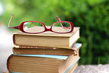 Stack of vintage books and reading glasses in a garden. Selective focus.
