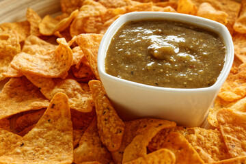 Bowl of roasted tomatillo salsa with tortilla chips. Smooth tomatillo dip to eat with nachos snack....