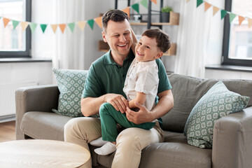 Obraz premium family, fatherhood and people concept - portrait of happy smiling father and little son sitting on sofa at home party