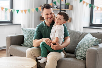 family, fatherhood and people concept - portrait of happy smiling father and little son sitting on sofa at home party