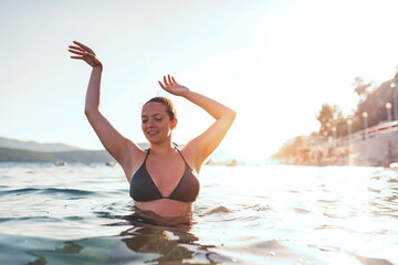 a beautiful woman in a swimsuit posing in the sea at sunset