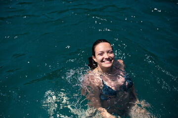 Beautiful woman in green bikini on tropical beach. Portrait of happy young woman smiling at sea. Brunette tanned girl in swimwear enjoying on beach.