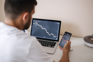 Young adult man trading on line with tablet pc connected to stock market. People, finance, investments. Over the shoulders