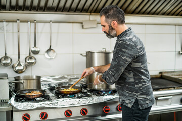 Professional cook is preparing meal in restaurant's kitchen. He is mixing food during frying.