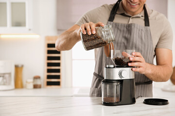 Man using electric coffee grinder in kitchen, closeup - obrazy, fototapety, plakaty