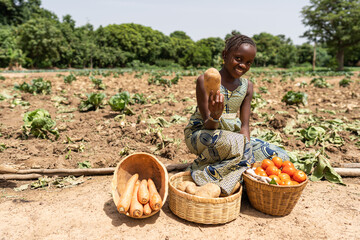 Beautiful little black African girl with a big smile on her face sitting on the roadside, offering...