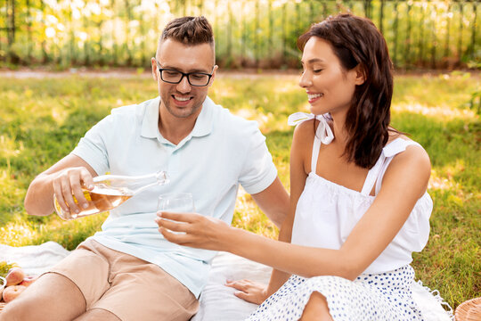 leisure and people concept - happy couple having picnic and pouring wine to glass at summer park