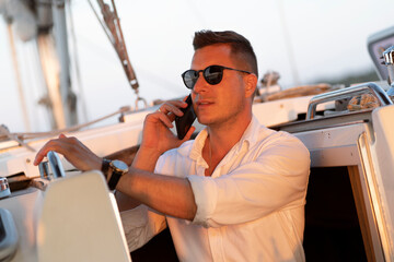 A successful man in a white shirt is talking on a mobile phone on a sailing yacht. As a concept of...