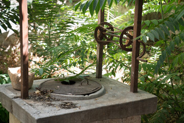Old historical water well with spinning wheel in green garden
