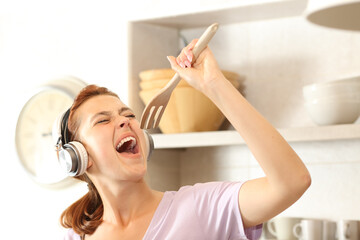 Happy woman listening to music singing in the kitchen