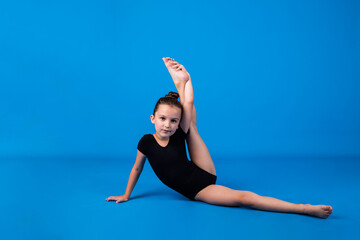 a little girl in a black swimsuit performs a gymnastic exercise on a blue background with a place for text