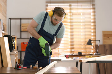 Obraz premium Carpenter working with electric drill at table indoors. Space for text
