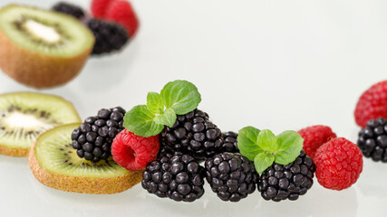 Fresh ripe blackberries, raspberries and kiwi slices with mint leaves scattered on a glass table.