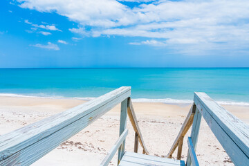 Access to the Atlantic Ocean along a boardwalk with a railing to the ocean in bright sunny weather in Florida