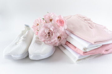 A stack of pink baby clothes and white sneakers. Toddler clothes set on white background with copy space decorated with pink flowers