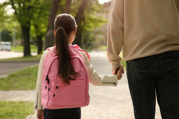 Father taking his little daughter to school through park, back view