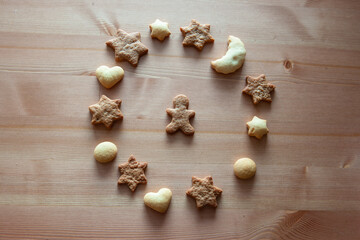 Different figures of ginger biscuits on a wooden table. Round pattern made of cookies on wooden background. Christmas cookies, stars, hearts, moon and gingerbread man is in the center