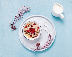 Muesli in a white bowl and a jug of milk on blue textured background with a white flowers