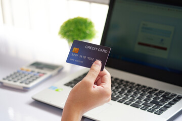 Female hand holding credit card and laptop computer on white desk. Concept of Online shopping and...