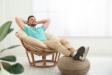 Handsome man relaxing in papasan chair at home, space for text