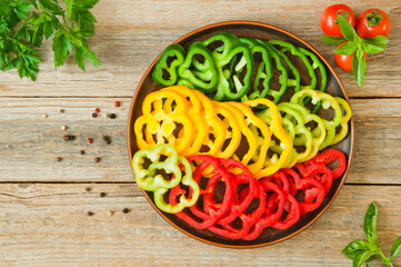 Multicolored slices of bell peppers on a plate on a wooden table