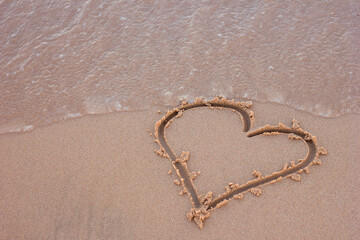 Heart symbol sign drawn on the sand of the ocean sea shore and a wave running over it