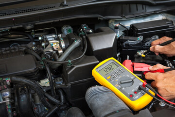 Car mechanic is using a multimeter with voltage range measurement to check the voltage level of the...