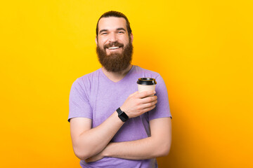 Bearded man on vibrant yellow color holding hot coffee in takeaway paper cup
