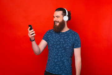 Photo of happy young bearded man using smartphone and wearing headphones, listening favorite music...